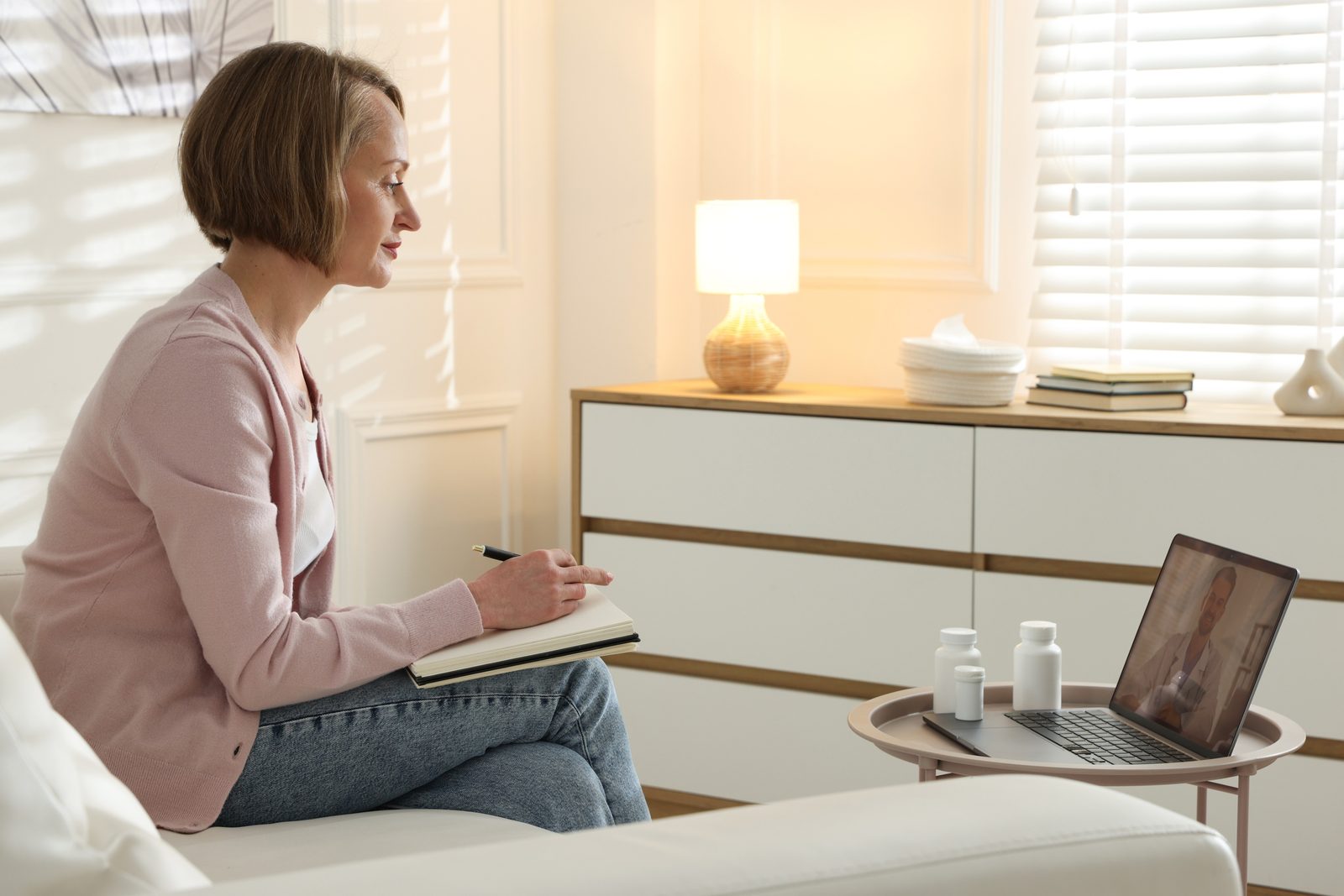 A woman in her fifties on a video call from her living room, notebook in hand